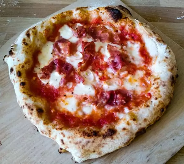 Neapolitan pizza with ham on wooden peel