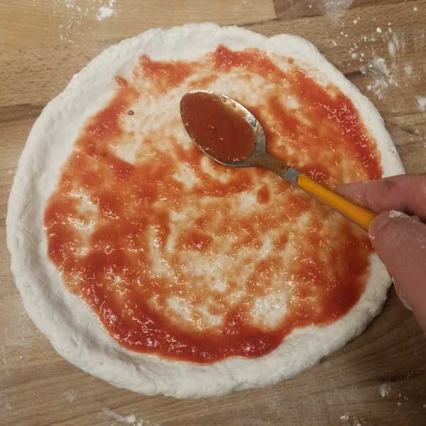 Spreading tomato sauce on NYC dough